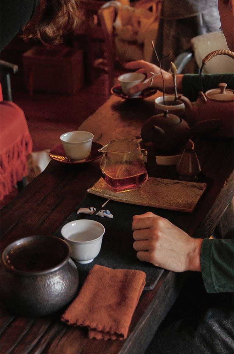 A close-up tea setting — teapots, cups, and tea brewing in a glass pot, photographed by EARTH.